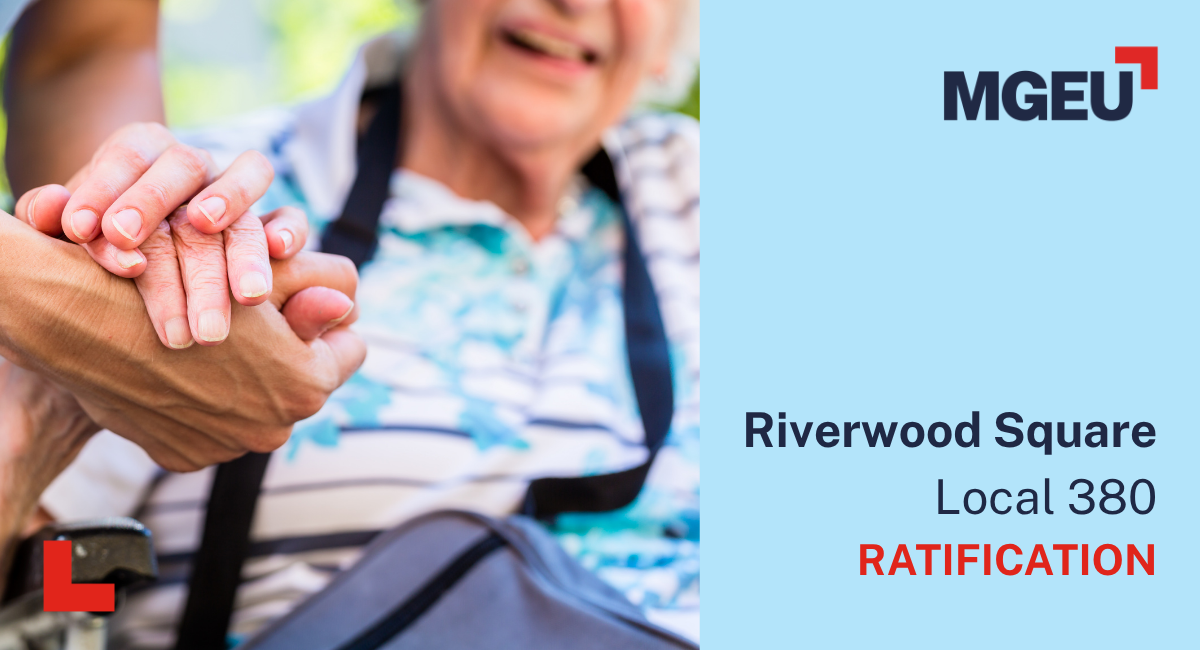An elderly person who is sitting clasps hands with a caregiver who is standing.